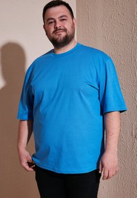 Modrá bavlnená tričko s krátkymi rukávmi, okrúhlym výstrihom, voľným strihom, hladkou textúrou a bez viditeľných vzorov. Nosené s čiernymi nohavicami.