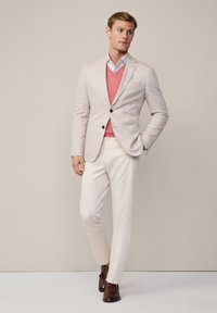 Blazer bej deschis, pulover corai cu decolteu în V, cămașă albastră deschisă, pantaloni crem și mocasini maro. Textură netedă, croială adaptată, design clasic.