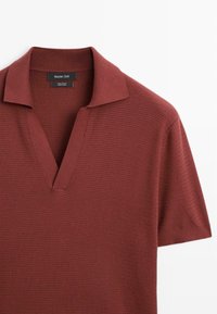 Polo a maniche corte di un profondo borgogna realizzato in cotone 100%. Presenta un collo a V, una trama texture e un design di collo classico.