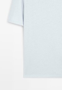 T-shirt bleu clair à manches courtes avec une texture simple et lisse, présenté sur un fond blanc, mettant en avant le détail de la manche et du côté.