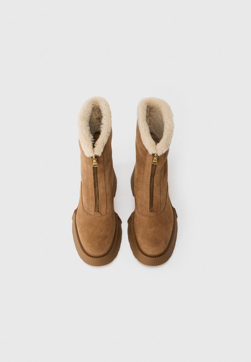 Bruine suede enkellaarzen hebben een crèmekleurige bontvoering, een rits aan de voorkant en een gestructureerde rubberen zool.