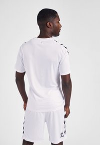 Weißes Sporttrikot und eine kurze Hose aus leichtem Material, mit schwarzen Akzenten und einem Logo auf der unteren rechten Seite der Hose.
