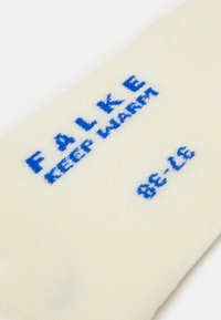 Light cream cotton sock with blue embroidery featuring the text “FALKE KEEP WARM” and size “86-116” visible. Smooth texture.