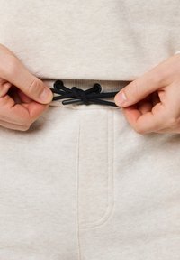 Ljust beige sweatpants har en dragsko i midjan, med svarta accenter och en mjuk textilstruktur, detaljerad sömnad och sidofickor.