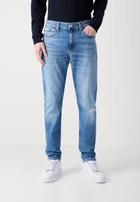 Ljusblå denimjeans med en avslappnad passform, som har ett subtilt blekt mönster och en slitning vid knäet, i kombination med vita sneakers.