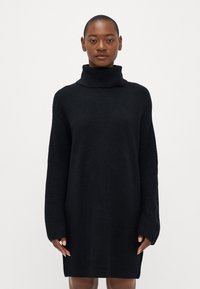 Melns adīts turtleneck kleita ar garām ribotu piedurknēm un brīvu piegriezumu, ar mīkstu tekstūru un vidukļa augstumu.