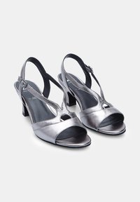 Srebrne sandały na obcasie typu slingback z błyszczącym metalicznym wykończeniem, otwartym noskiem, krótkim słupkiem i wycięciami po bokach.