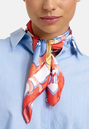 Frau trägt ein hellblaues Hemd mit Knöpfen und ein buntes Seidenschal in Rot, Blau und Orange, das um ihren Hals gebunden ist.