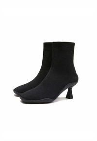 Bottines noires en tissu extensible avec un haut côtelé, un bout pointu et un talon aiguille court et angulaire. Texture lisse sur l'ensemble.
