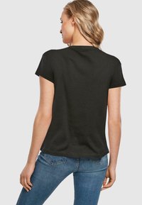 Sort t-shirt med korte ærmer og rund halsudskæring, lavet af blødt stof. Kanten er let buet, og den er parret med blå jeans.