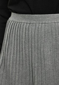 Šedá plisovaná sukně z měkké pletené látky. Má strukturovaný pas a svislé žebrování, které poskytují volnější střih a neformální vzhled.