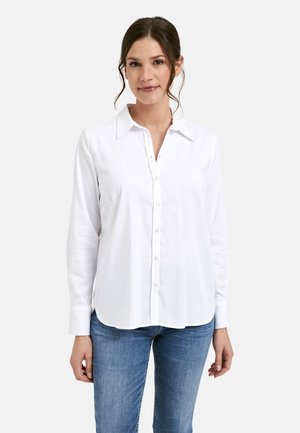 White long-sleeve button-up shirt with a collar, featuring a smooth fabric texture and a curved hem. Paired with blue jeans.
