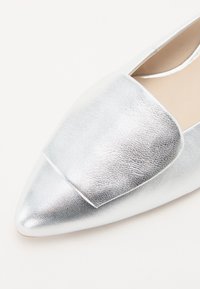 Sudraba metāla loaferi ar gludu, teksturētu virsmu, smailu purngalu un elegantu dizainu. Iezīme plata, plakanā josta augšdaļā.