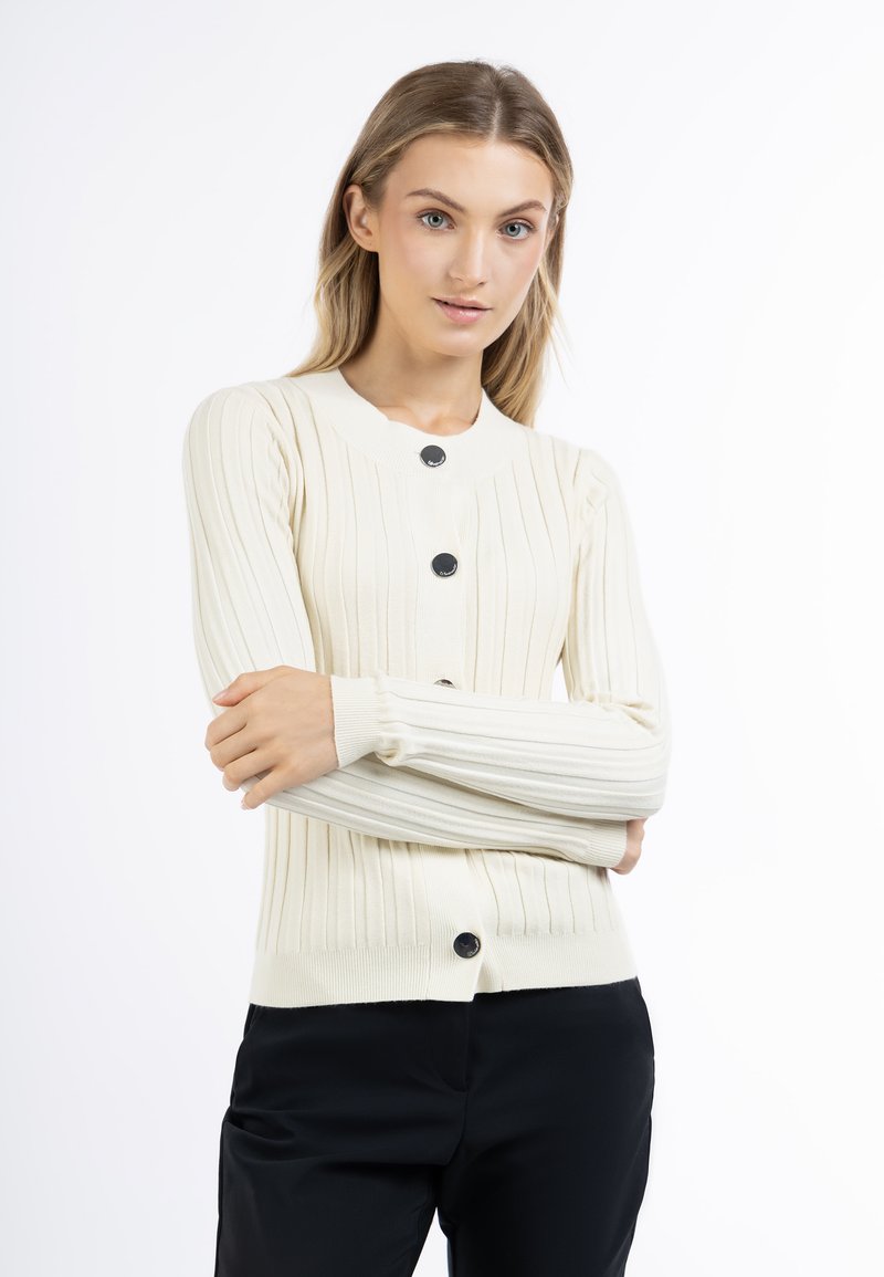 Cardigan a coste crema con maniche lunghe, scollatura rotonda e bottoni neri sul davanti. Texture morbida, design aderente e silhouette strutturata.