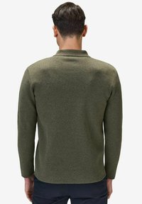 Grön stickad långärmad polo med krage, med en slät textur och en rundad nederkant, visad från en bakvy.