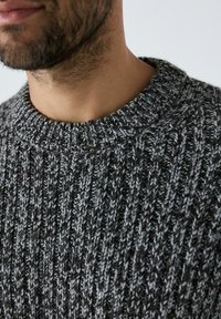 Pulover gri tricotat, cu o textură țesută și un design clasic cu gât rotund, realizat dintr-un amestec de fire gri închis și gri deschis.