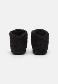 Black fleece slippers with a textured exterior, featuring a rounded shape and cuffed tops, designed for comfort and warmth.