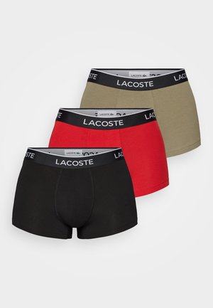 Drei Paar Lacoste Boxer Shorts in Schwarz, Rot und Olivgrün. Jedes Paar hat einen schwarzen Bund mit dem Lacoste-Logo. Aus Baumwollmaterial.