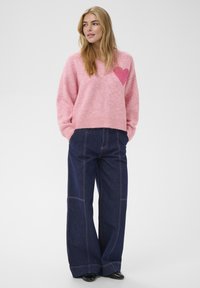 Pull en tricot rose avec un motif de cœur rose contrastant, associé à un pantalon en denim bleu foncé ample avec des détails de couture visibles.