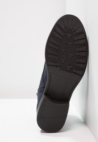 Scarpa navale con suola in gomma nera testurizzata che presenta un battistrada con motivo e un design superiore cucito. Dettaglio della zip laterale visibile.