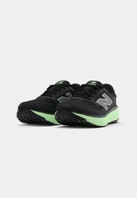 Must have mustadest velged mustad New Balance jooksujalatseid kerge rohelise pehmendusega tallaga, esitatud valge tausta ees.