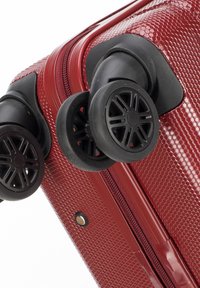 Rode hard-shell bagage met een gestructureerd hexagonaal patroon, uitgerust met twee zwarte dubbele wielen en een stoffen ritsloper langs de naad.