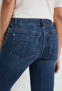 Jeans de mezclilla azul oscuro con un diseño de talle alto, que cuentan con dos bolsillos traseros y sutiles detalles de costura a lo largo de la cinturilla.