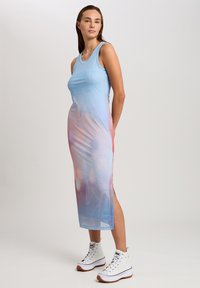 Ärmelloses Maxikleid in einem Farbverlauf von Blau zu Pink mit floralem Muster. Aus glattem, leichtem Material mit seitlichen Schlitzen. Kombiniert mit weißen High-Top-Sneakern.