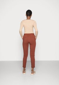 Top a maniche lunghe beige a costine abbinato a pantaloni tapered color ruggine, dotati di una cintura elastica, polsini arrotolati e tasche posteriori.