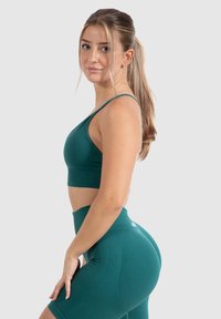 Conjunto de entrenamiento en color teal que incluye un sujetador deportivo con tirantes y shorts de cintura alta. La tela es suave, con una textura acanalada y un detalle de marca mínimo.