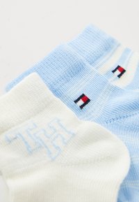 Calze di cotone azzurro chiaro e bianche. La calza blu presenta strisce orizzontali e un logo, mentre la calza bianca ha una grafica azzurro chiaro.