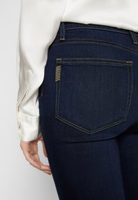 Jeans de mezclilla azul oscuro con una forma ajustada. Presentan un bolsillo trasero con costuras en contraste y una textura de tela suave.