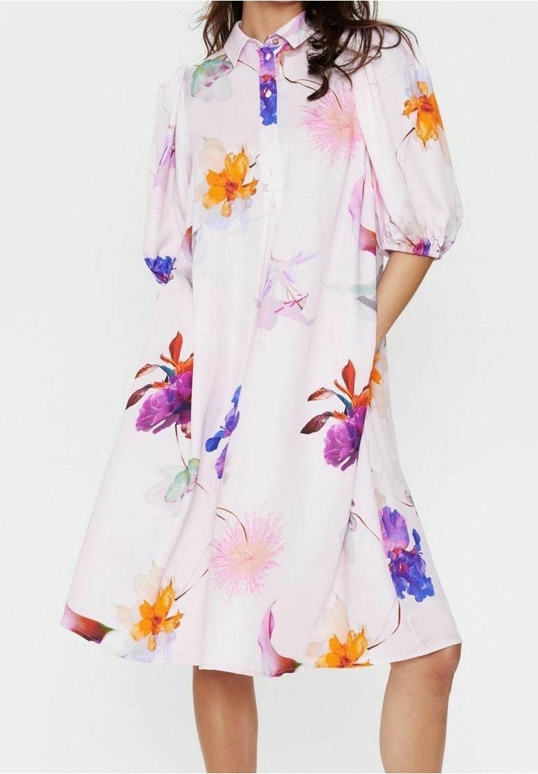 Robe midi blanche avec manches bouffantes et imprimé floral dans des tons orange, violet, rose et bleu, portée par une personne debout.