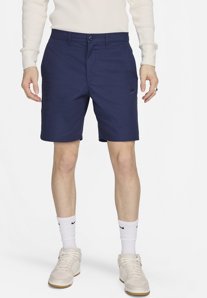 Pantalones cortos azul marino con cierre de botón, bolsillos laterales y un sutil logo de Nike. Fabricados con una tela suave y de corte relajado.