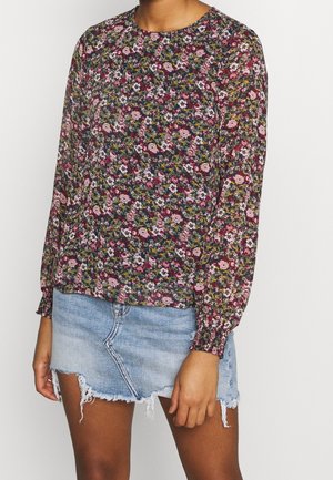 Blusa floreale a maniche lunghe in colori scuri con scollatura rotonda, polsini arricciati e un tessuto leggero e trasparente sopra una mini gonna di denim.