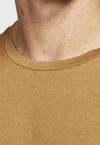 Kurzärmliges Rundhals-T-Shirt aus strukturiertem, senfgelbem Stoff mit einem glatten Halsausschnitt und subtilen gesprenkelten Mustern.