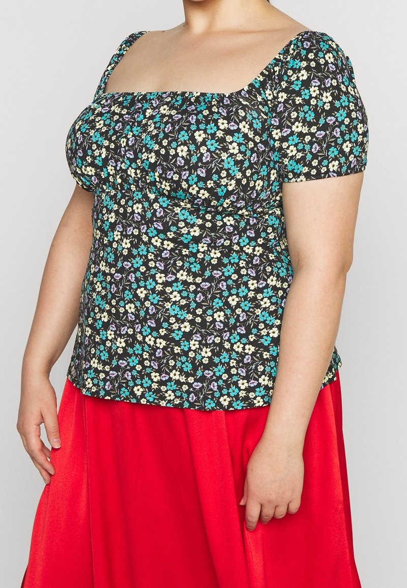 Haut noir à motifs floraux avec des manches bouffantes, ornée de fleurs teal, violettes et jaunes ; décolleté carré et design ajusté. Assorti à une jupe rouge.