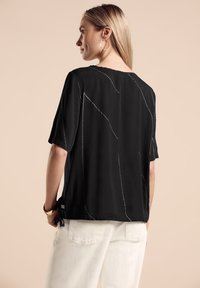 Blusa nera a maniche corte con motivi di cucitura bianca, caratterizzata da una vestibilità ampia e un colletto rotondo. I lacci ai lati migliorano il design.