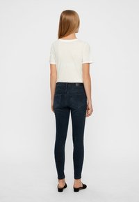 Jeans skinny de color azul oscuro con una cintura alta, que cuentan con bolsillos traseros y una textura suave, combinados con una camiseta de color claro.