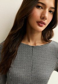 Zwart-wit houndstooth patroon jurk met een ronde halslijn en korte mouwen, met een gladde stofstructuur en subtiele naden.