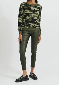 Fuzzy grön kamouflage tröja med rund halsringning, i kombination med figurnära mörkgröna läderbyxor. Svarta loafers med gyllene detaljer.