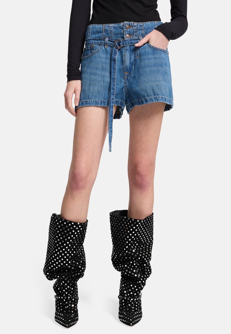 Shorts in denim con vita con cintura, orlo sfrangiato e due tasche frontali. Abbinati a stivali lucidi neri al ginocchio con pois argentati.