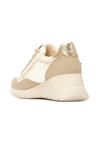 Zapatilla beige con un acabado de cuero y ante suave, que presenta un acento metálico dorado en el talón y una suela gruesa y esculpida.