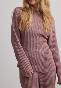 Maglione a coste rosa con maniche lunghe e orlo dritto. Presenta un knit strutturato e una vestibilità rilassata, abbinato a pantaloni coordinati.