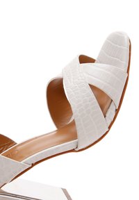 Sandalo bianco con texture a rilievo effetto coccodrillo, dotato di cinturini incrociati e suola marrone. Il design è minimalista e con punta aperta.