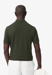 Mörkgrön kortärmad polo t-shirt i lätt material, med krage och figurnära design. Bakifrån visar den en slät textur.