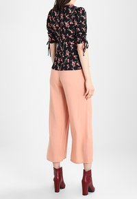 Camicia nera a fiori con maniche a sbuffo; abbinata a pantaloni a gamba larga color pesco. La modella indossa stivaletti marsala con dettagli borchiati.