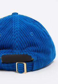 Gorra de béisbol de pana azul con correa ajustable y hebilla dorada grabada con "BIMBA Y LOLA" sobre un fondo blanco.