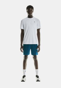 White short-sleeve athletic t-shirt with logo, paired with blue shorts. Model wears white crew socks and black sneakers with gray accents.