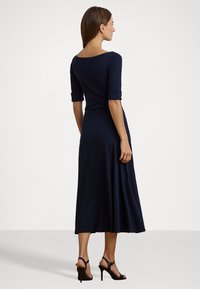 Navy blue, knee-length dress with a scoop back, three-quarter sleeves, and flared skirt. Pair of black strappy heels.